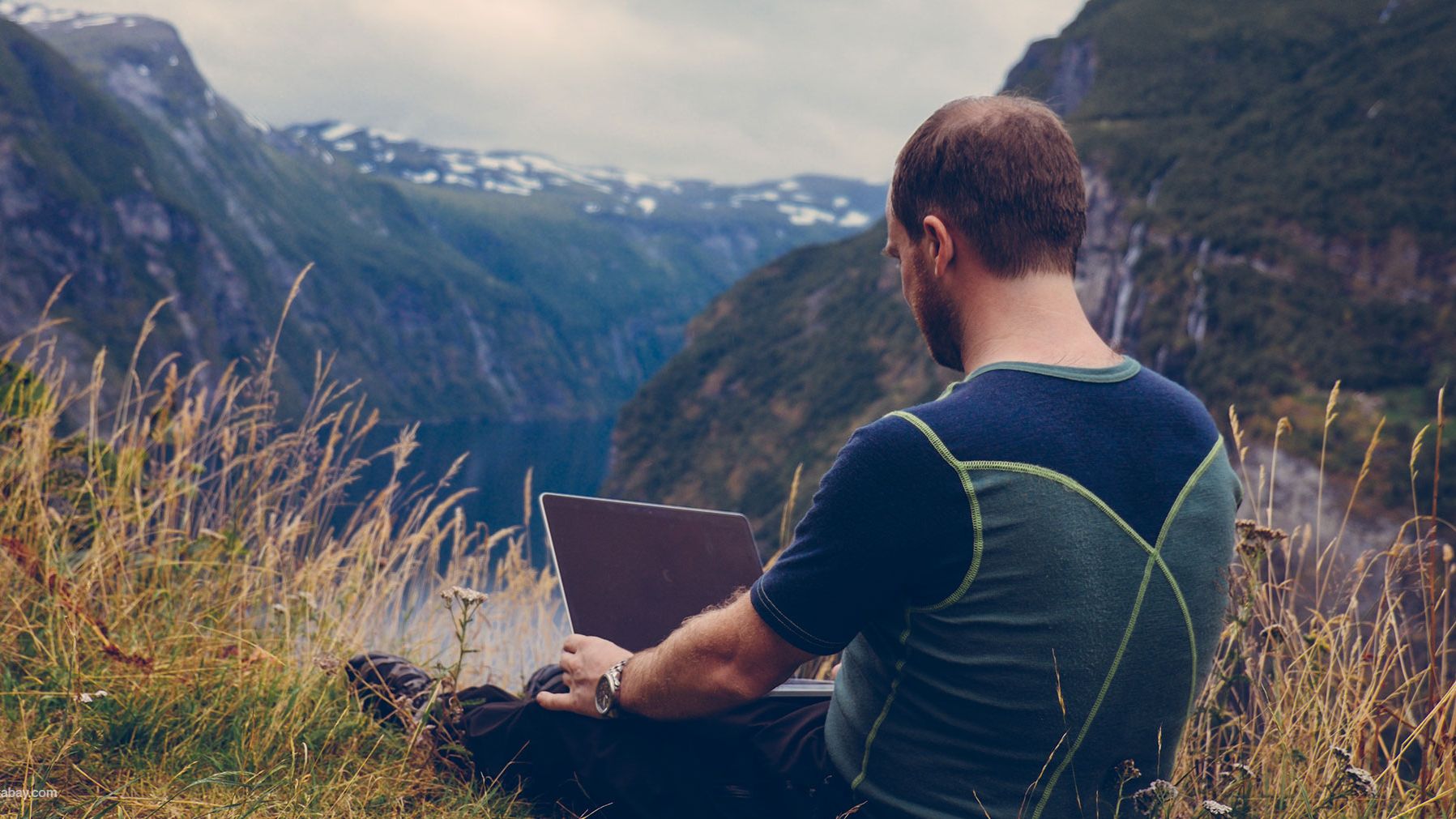 ein Mann sitzt mit einem Laptop auf einem Berg